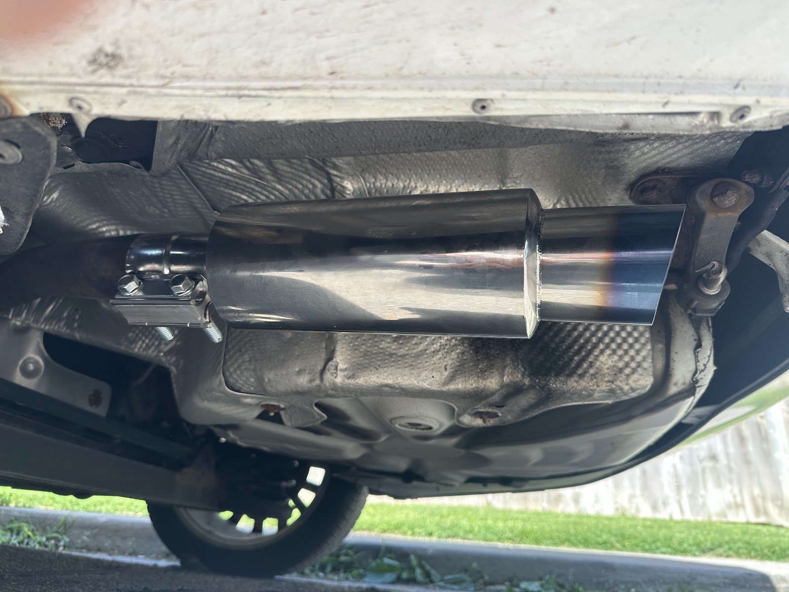 A polished stainless exhaust tip mounted under the rear of a vehicle on the lift.